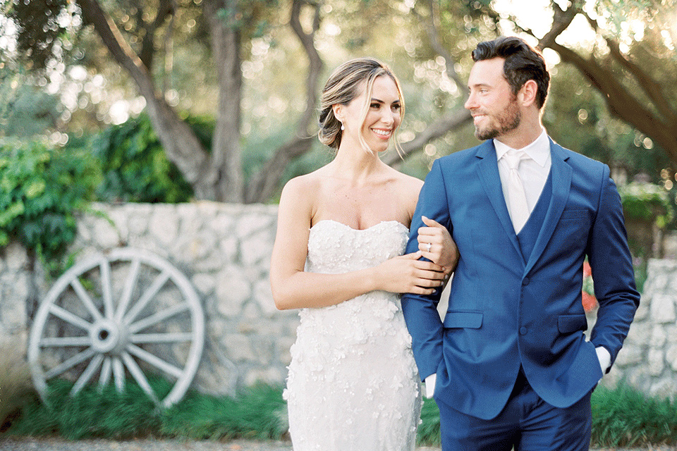 whispering-rose-shoot-bride-and-groom-walking-towards-the-camera-bride-wearing-a-strapless-gown-with-pink-shoes-groom-in-a-cobalt-blue-suit-with-brown-shoes-and-an-ivory-tie