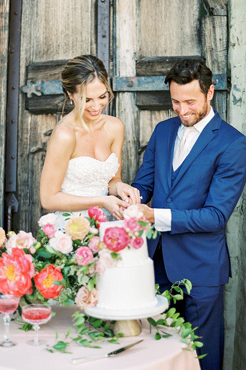 whispering-rose-shoot-bride-and-groom-with-cake-bride-wearing-a-strapless-gown-with-pink-shoes-groom-in-a-cobalt-blue-suit-with-brown-shoes-and-an-ivory-tie