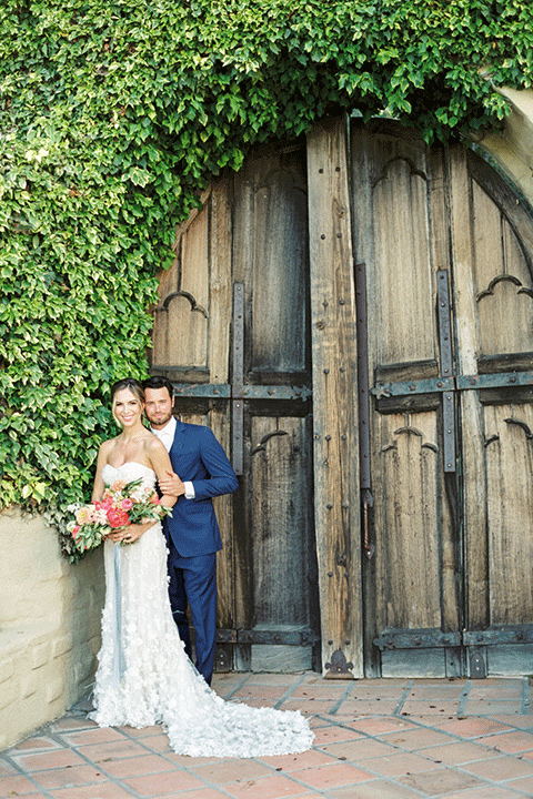 whispering-rose-shoot-couple-by-wooden-door-bride-wearing-a-strapless-gown-with-pink-shoes-groom-in-a-cobalt-blue-suit-with-brown-shoes-and-an-ivory-tie