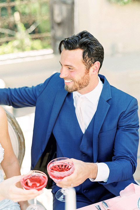 whispering-rose-shoot-groom-with-drink-bride-wearing-a-strapless-gown-with-pink-shoes-groom-in-a-cobalt-blue-suit-with-brown-shoes-and-an-ivory-tie