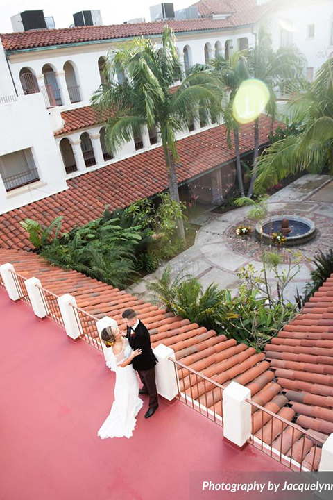  bride wearing white pointed toe shoes and a white long gown with flowing sleeves and a high neckline and the groom in a black velvet tuxedo embacing