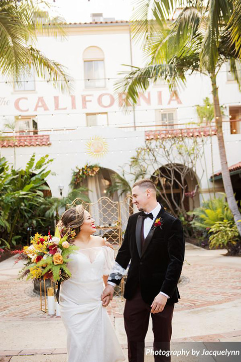  bride in a white silk gown with flowing sleeves and a high neckline and the groom in a black velvet tuxedo walking