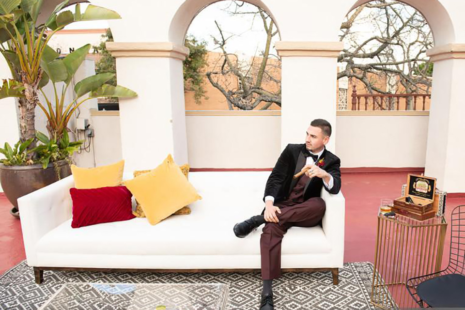  groom sitting on a couch in a black velvet tuxedo