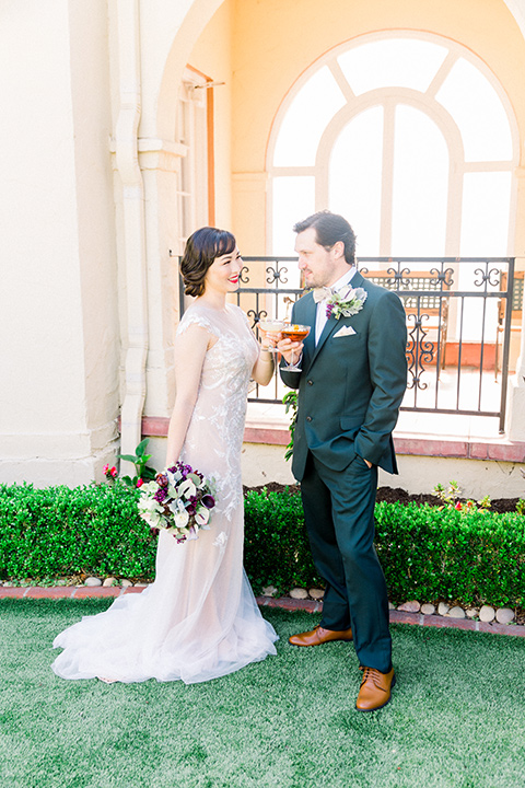  bride in a Spanish style white lace gown with sleeves and dee red lipstick groom in a deep green suit with a tan bow tie