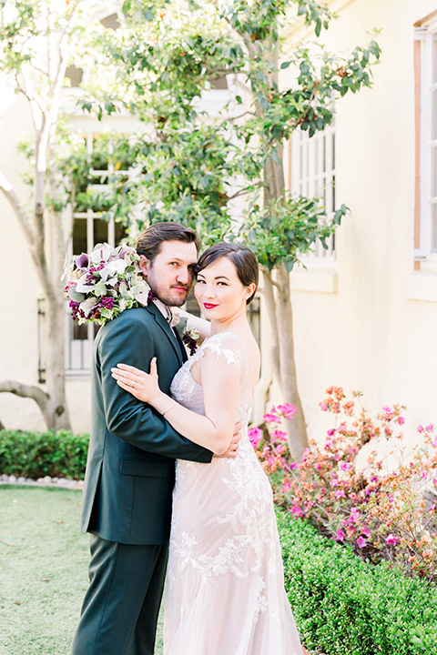  bride in a Spanish style white lace gown with sleeves and dee red lipstick and the groom in a dark green suit with a tan bow tie and brown shoes
