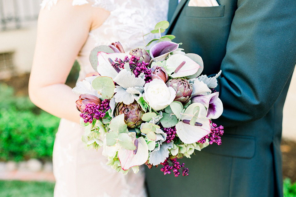  bride in a Spanish style white lace gown with sleeves and dee red lipstick and the groom in a dark green suit with a tan bow tie and brown shoes holding flowers