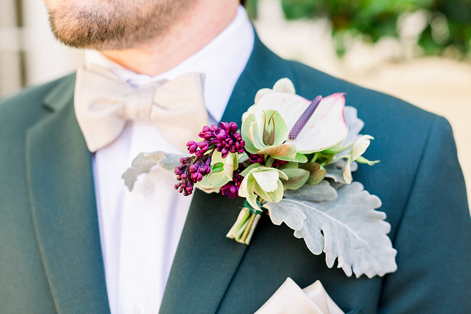  the groom in a dark green suit with a tan bow tie and brown shoes
