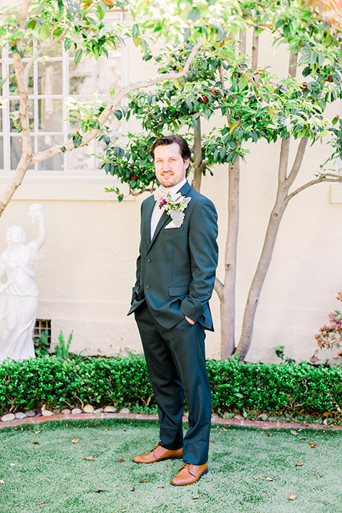  the groom in a dark green suit with a tan bow tie and brown shoes