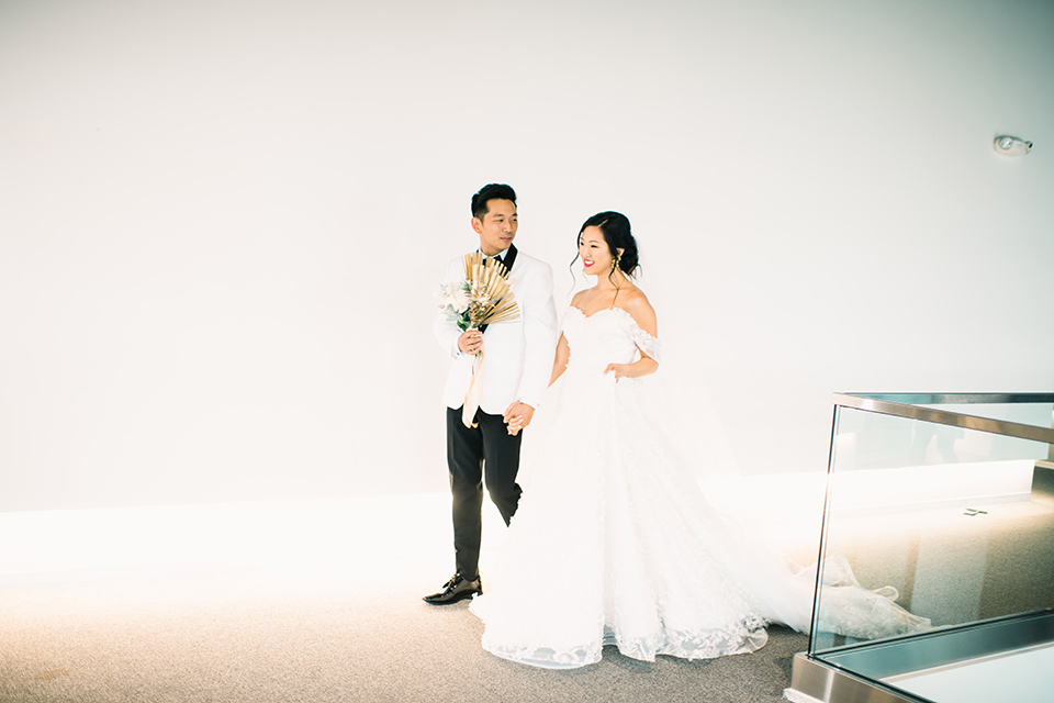  bride in a white gown with a strapless neckline and the groom in an ivory paisley tuxedo with a black bow tie walking