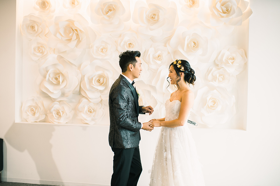 bride in a white gown with a strapless neckline and the groom in an ivory paisley tuxedo with a black bow tie at ceremony