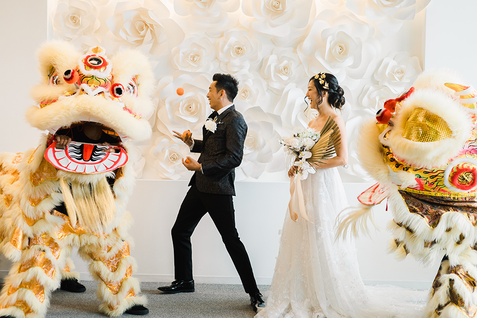  bride in a white gown with a strapless neckline and the groom in an ivory paisley tuxedo with a black bow tie with dragons outside