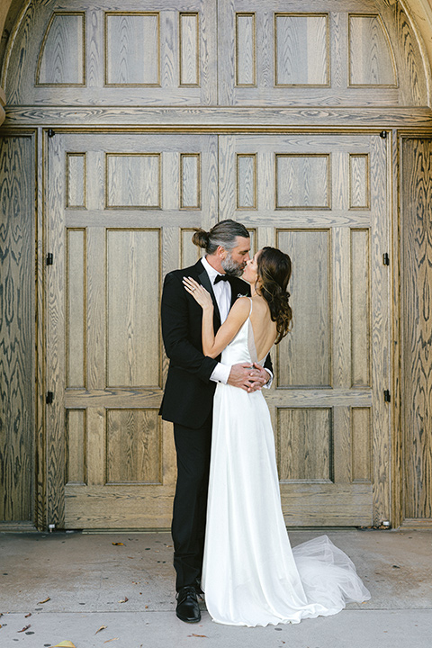  bride in a satin formfitting gown with thin straps, and the groom in a black notch lapel tuxedo with a black bow tie