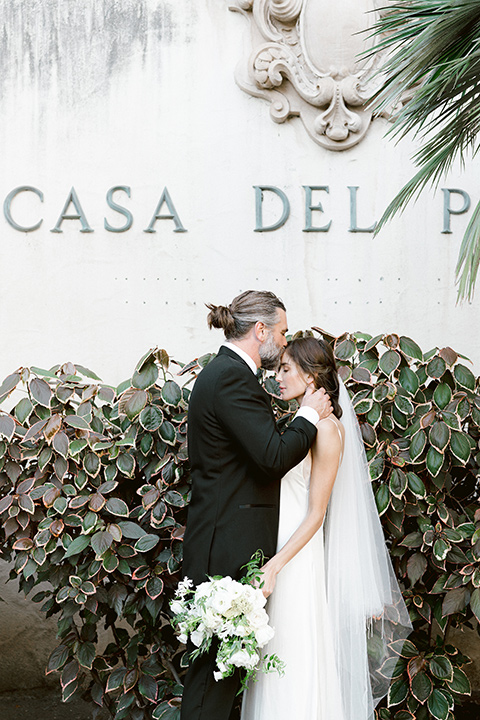  bride in a satin formfitting gown with thin straps, and the groom in a black notch lapel tuxedo with a black bow tie 