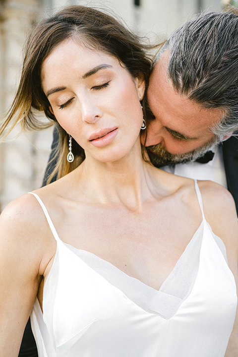  bride in a satin formfitting gown with thin straps, and the groom in a black notch lapel tuxedo with a black bow tie 