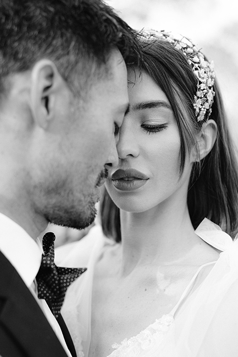  bride in a white lace gown with a flowing skirt with a high slit on the side, and tie straps.  The groom in a black michael kors tuxedo with a black bow tie 