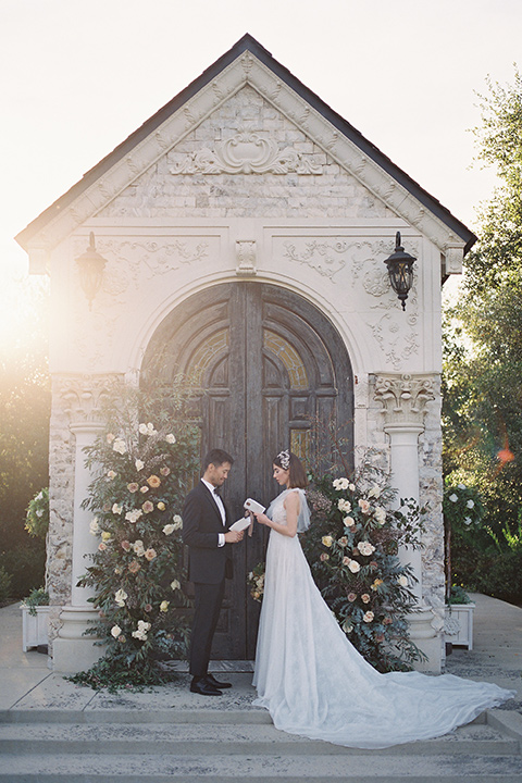  bride in a white lace gown with a flowing skirt with a high slit on the side, and tie straps.  The groom in a black michael kors tuxedo with a black bow tie 