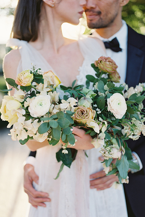  bride in a white lace gown with a flowing skirt with a high slit on the side, and tie straps.  The groom in a black michael kors tuxedo with a black bow tie 