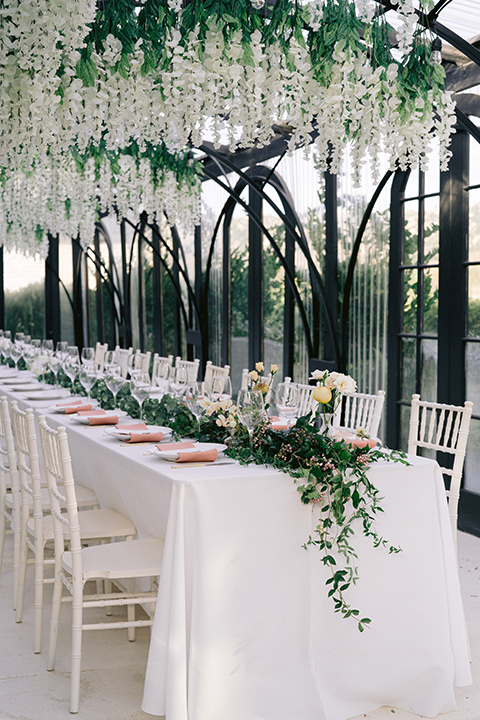  bride in a white lace gown with a flowing skirt with a high slit on the side, and tie straps.  The groom in a black michael kors tuxedo with a black bow tie 