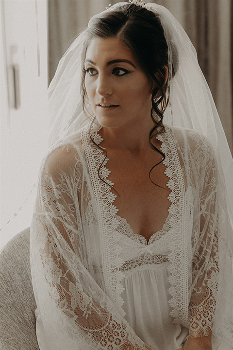 bride in a white lace robe getting her hair and makeup done