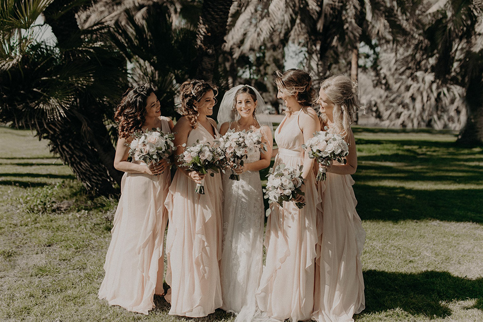  bride in a modern white gown with a v neckline and lace detailing and the bridesmaids in pink gowns 