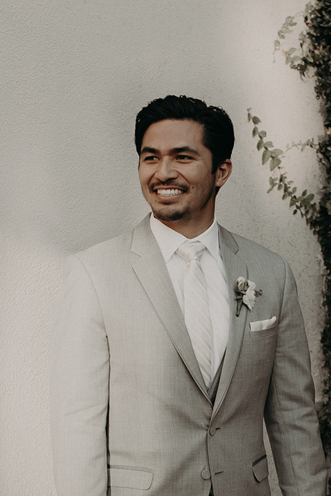  the groom in a light grey suit with a white long tie and brown shoes 