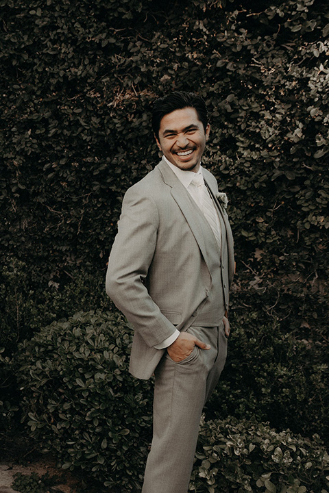  the groom in a light grey suit with a white long tie and brown shoes