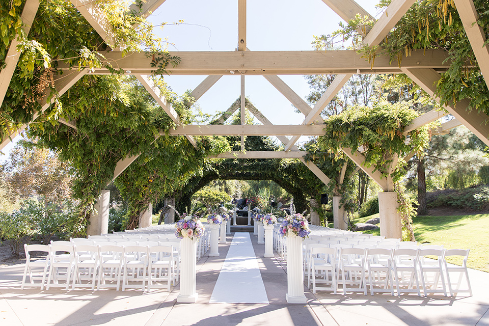  bride in a white gown with an off the shoulder neckline and the groom in a light blue suit with a blue bow tie, the groomsmen in light blue suits and the bridesmaids in lilac colored gowns 