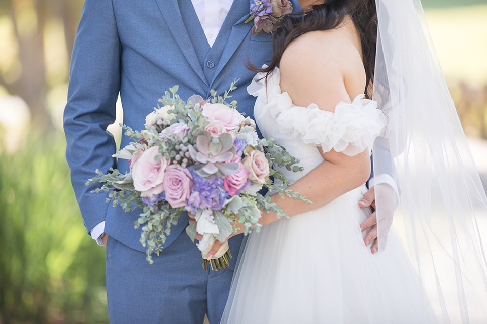  bride in a white gown with an off the shoulder neckline and the groom in a light blue suit with a blue bow tie