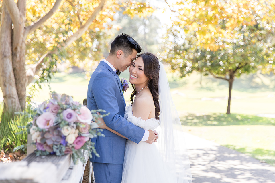  bride in a white gown with an off the shoulder neckline and the groom in a light blue suit with a blue bow tie