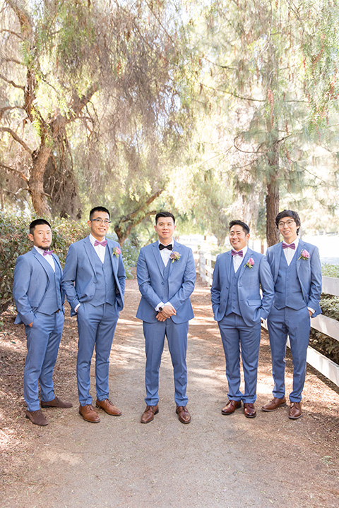  bride in a white gown with an off the shoulder neckline and the groom in a light blue suit with a blue bow tie, the groomsmen in light blue suits and the bridesmaids in lilac colored gowns