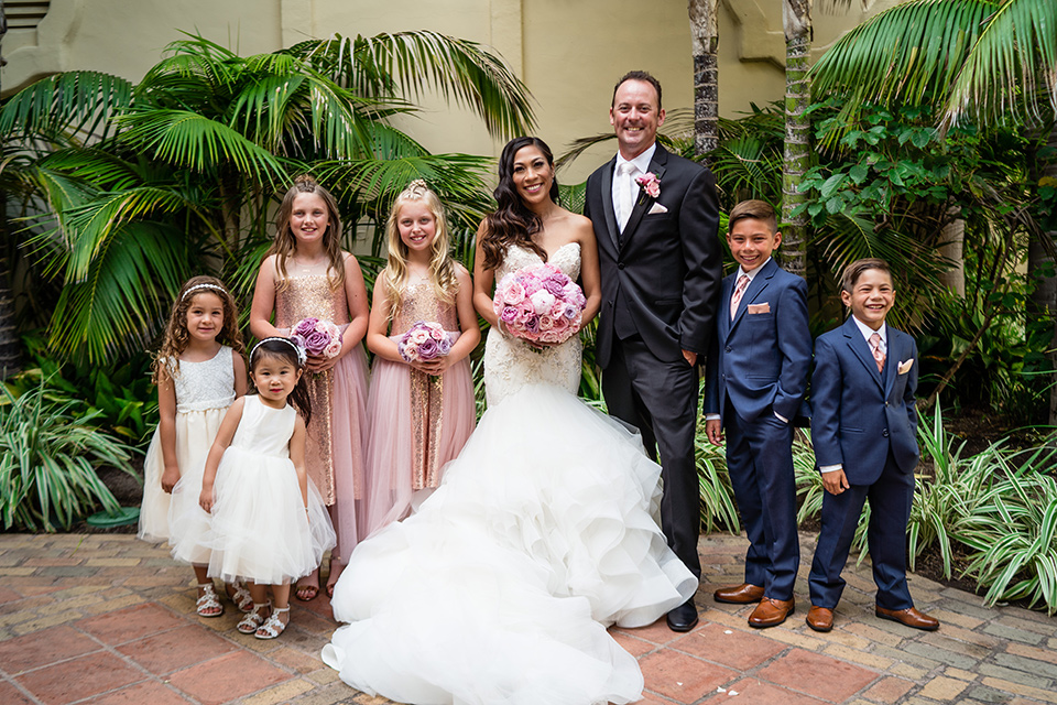  The bride in a mermaid style gown with a sweetheart neckline and the groom in a black tuxedo with a white long tie with their children 