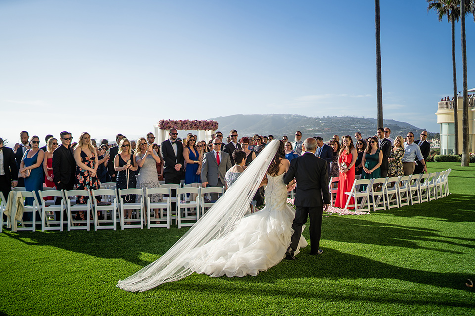  The bride in a mermaid style gown with a sweetheart neckline walking down the aisle with her father 