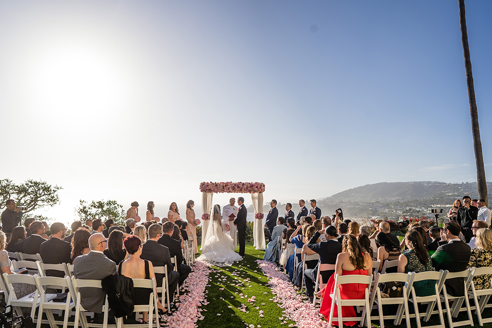  The bride in a mermaid style gown with a sweetheart neckline and the groom in a black tuxedo with a white long tie at their ceremony 