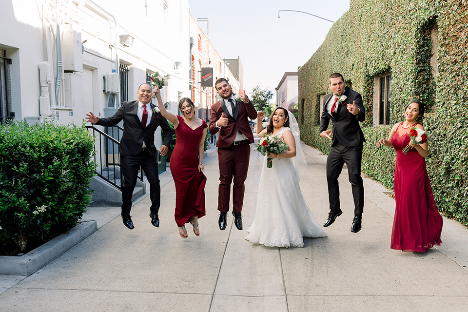  the bride in a lace a line gown with tulle cap sleeves and a modified sweetheart neckline, the groom in burgundy tuxedo with a shawl lapel tuxedo with a black long tie.  The groomsmen in black and grey suits with burgundy long tie and the bridesmaids in wine and burgundy long gowns