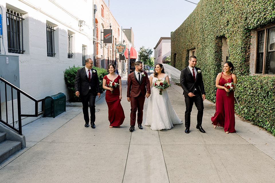  the bride in a lace a line gown with tulle cap sleeves and a modified sweetheart neckline, the groom in burgundy tuxedo with a shawl lapel tuxedo with a black long tie.  The groomsmen in black and grey suits with burgundy long tie and the bridesmaids in wine and burgundy long gowns