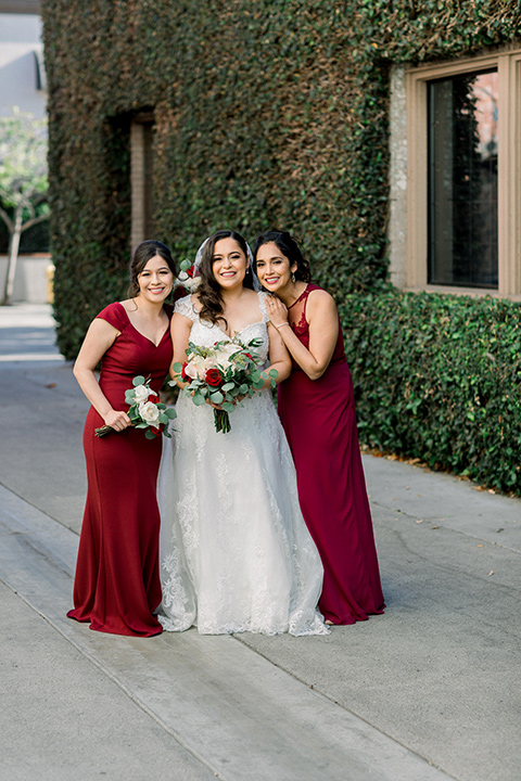  the bride in a lace a line gown with tulle cap sleeves and a modified sweetheart neckline and the bridesmaids in wine and burgundy long gowns