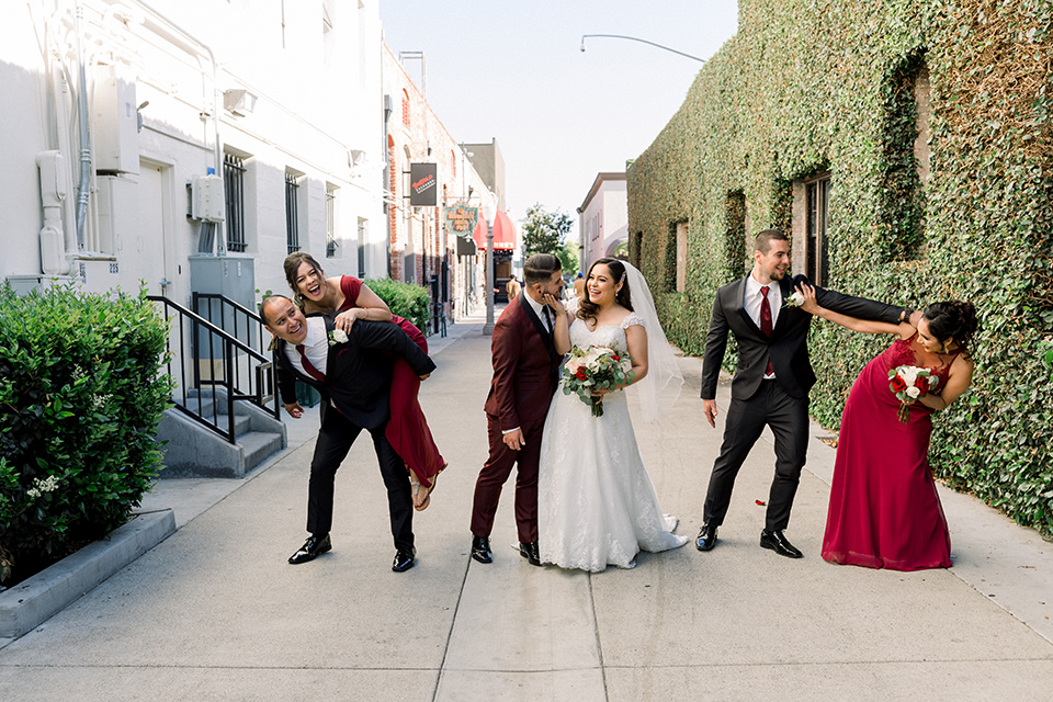  the bride in a lace a line gown with tulle cap sleeves and a modified sweetheart neckline, the groom in burgundy tuxedo with a shawl lapel tuxedo with a black long tie.  The groomsmen in black and grey suits with burgundy long tie and the bridesmaids in wine and burgundy long gowns