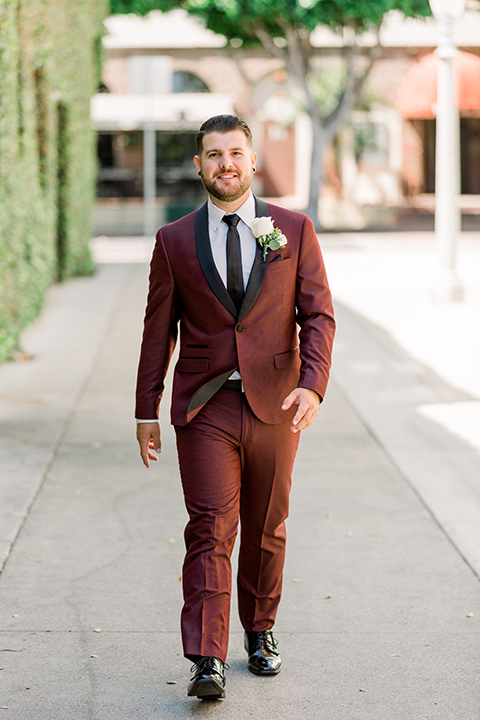  the groom in burgundy tuxedo with a shawl lapel tuxedo with a black long walking towards camera