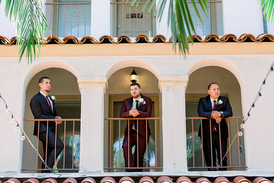  the groom in burgundy tuxedo with a shawl lapel tuxedo with a black long tie, The groomsmen in black and grey suits with burgundy long ties