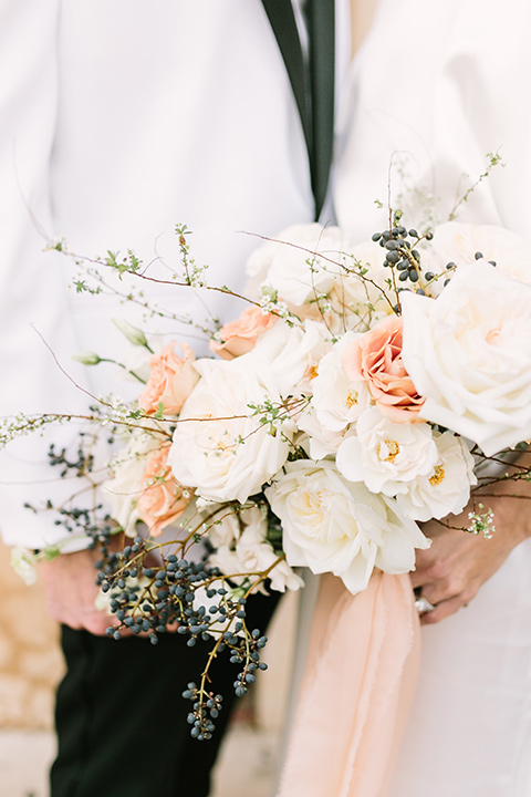  bride in a white gown with a high neckline and gold headpiece and the groom in a white shawl lapel tuxedo with a black bow tie