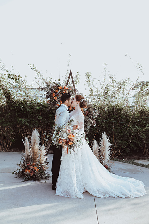  the bride is in a white flowing gown with a lace sleeves and a high neck line, and the groom in a grey jacket with black pants 