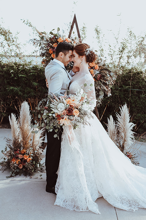 the bride is in a white flowing gown with a lace sleeves and a high neck line, and the groom in a grey jacket with black pants