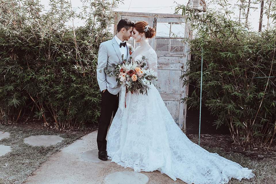  the bride is in a white flowing gown with a lace sleeves and a high neck line, and the groom in a grey jacket with black pants 