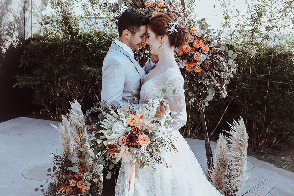  the bride is in a white flowing gown with a lace sleeves and a high neck line, and the groom in a grey jacket with black pants 