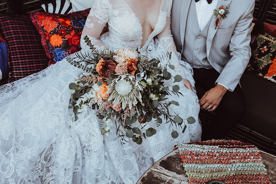 the bride is in a white flowing gown with a lace sleeves and a high neck line, and the groom in a grey jacket with black pants 
