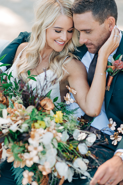  bride in a white lace bohemian style wedding gown with a tan wide brimmed hat and the groom in a dark green suit with a chocolate long tie 