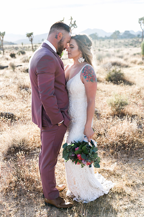  bride in a white lace bohemian style gown with a sweetheart neckline and thin straps and the groom in a rose pink suit with a burgundy bow tie