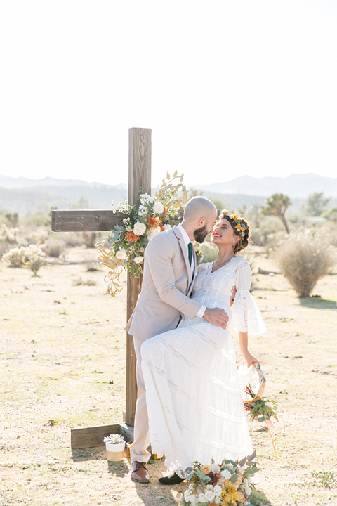  bride in a bohemian style gown with lace and a floral crown, the groom in a tan suit with a teal long tie 