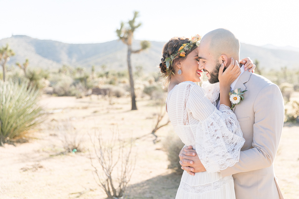  bride in a bohemian style gown with lace and a floral crown, the groom in a tan suit with a teal long tie kissing