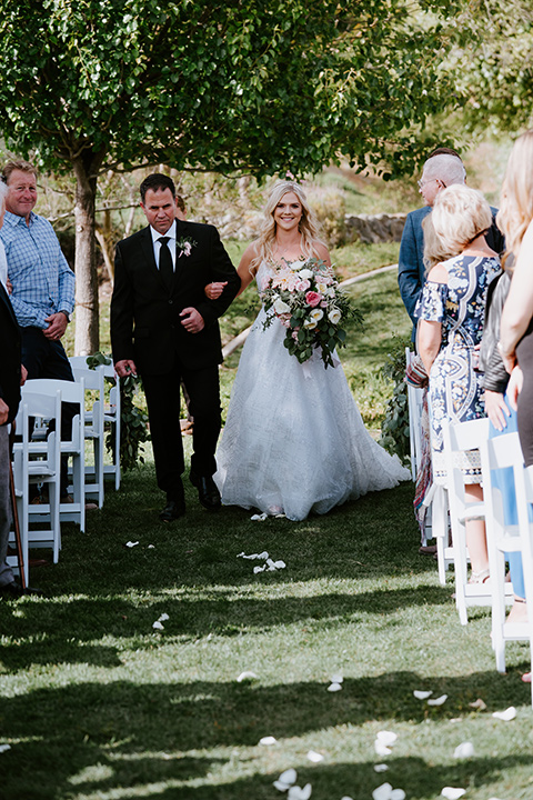 bride in a white ballgown with a strapless neckline and a long veil and jean jacket, and the groom in a notch lapel tuxedo and black bow tie kissing with the sparklers